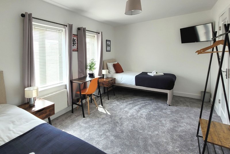 Bright bedroom with two single beds, wooden desk, chair, mounted TV and large windows