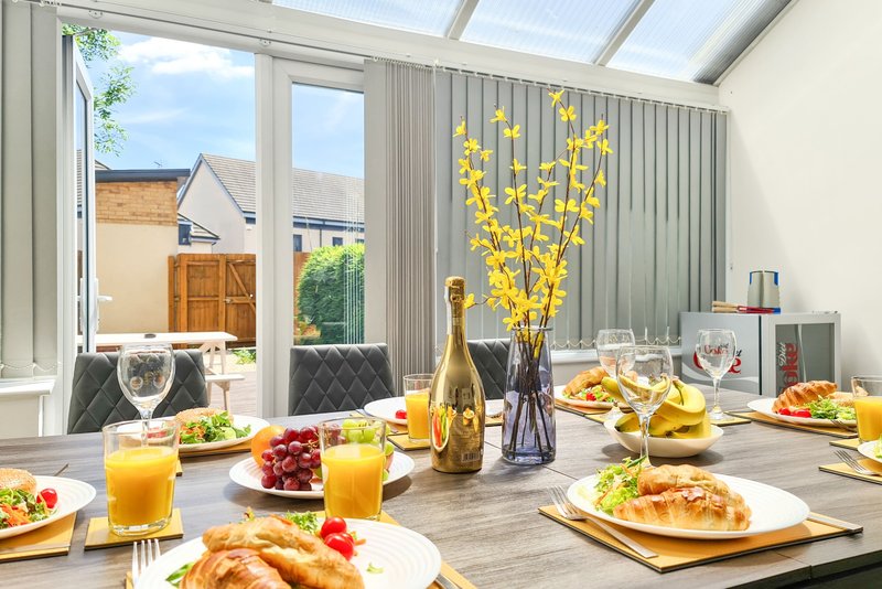 Modern dining room with set table, champagne bottle, yellow flowers, and garden view through windows