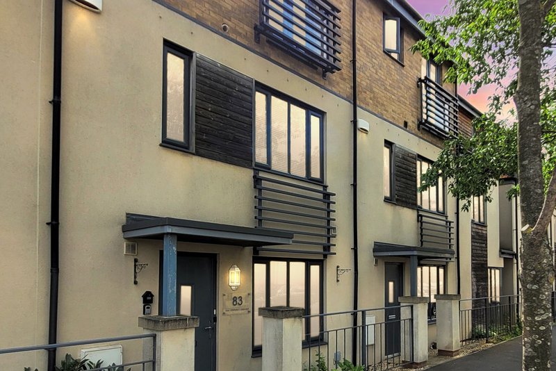 Modern terraced townhouses with cream and black facade, metal balconies, and climbing ivy