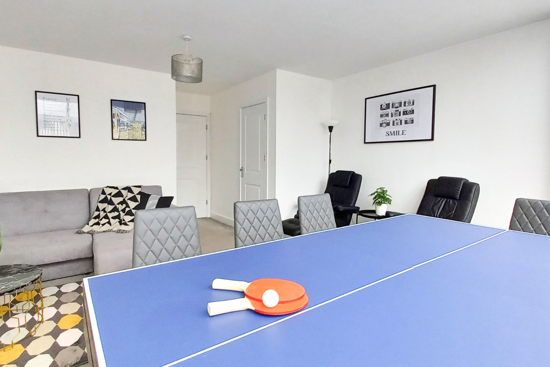 Recreation room with blue ping-pong table, paddles, sofa, chairs and wall art