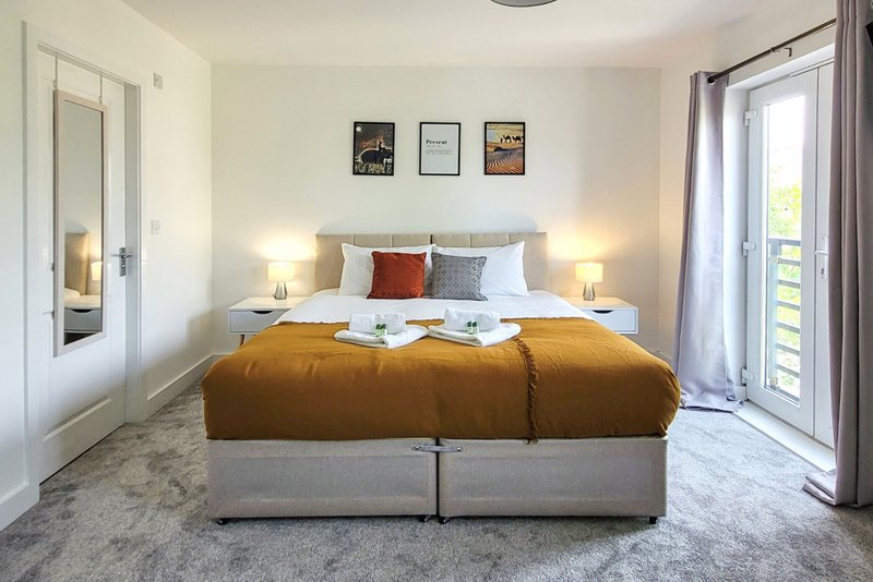 Bright bedroom with double bed, mustard throw, bedside lamps, wall art and glass doors
