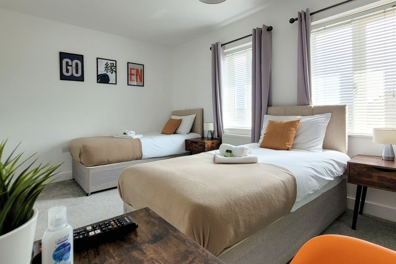 Bright twin bedroom with two single beds, beige bedding, framed wall art, and natural light from windows