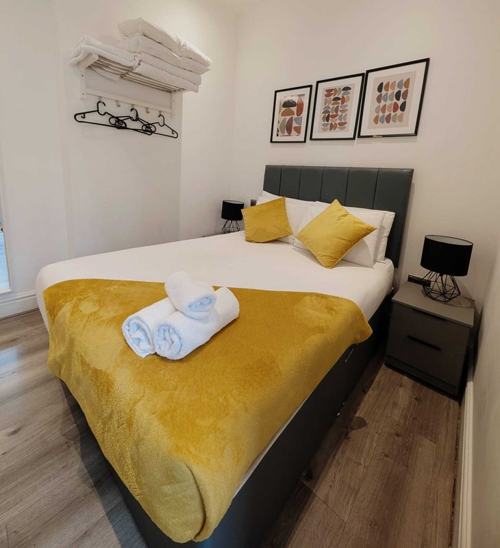 Bedroom with double bed, yellow bedding, black headboard, bedside table and wall art