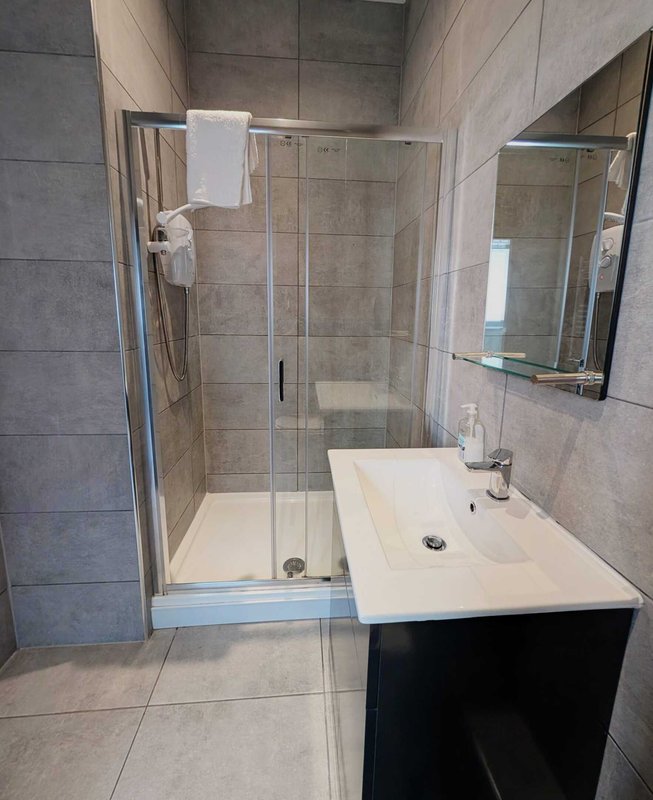 Modern bathroom with walk-in shower, white sink, mirror and grey tile walls
