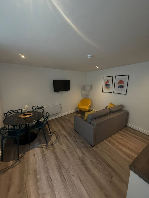 Open-plan living room with grey sofa, dining table, wall-mounted TV and wooden flooring