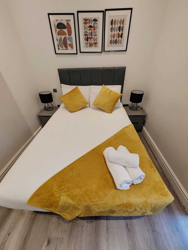 Modern bedroom with double bed, yellow bedding, black headboard and framed wall art