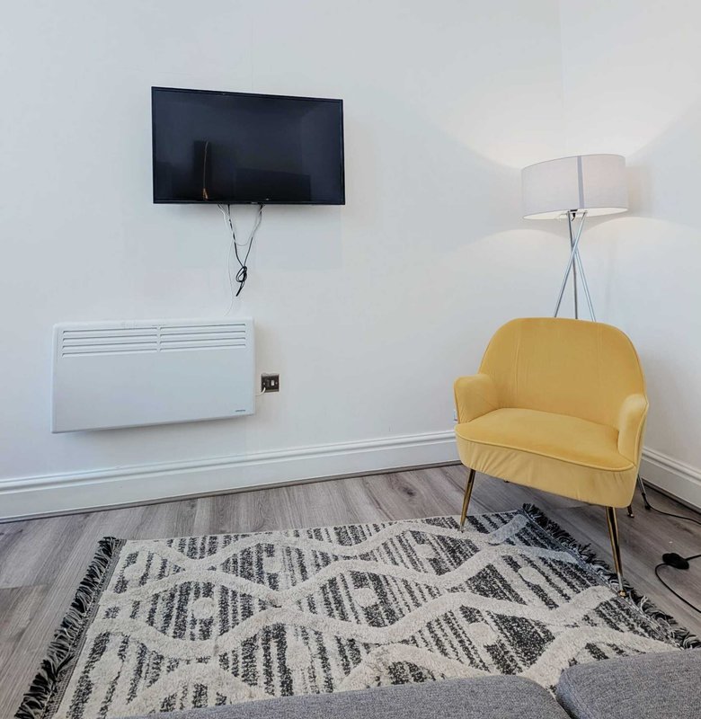 Modern living room with yellow armchair, wall-mounted TV, geometric patterned rug and floor lamp