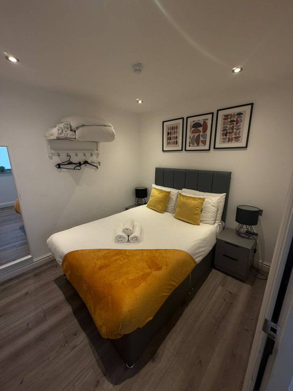 Modern bedroom with double bed, yellow throw, black headboard and framed wall art