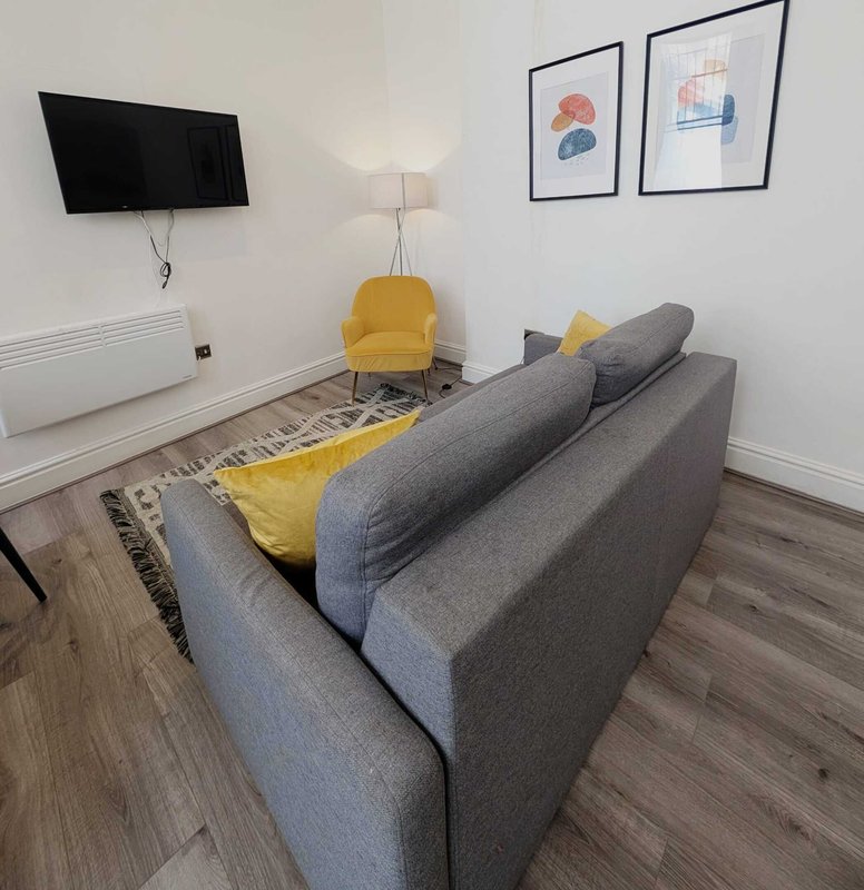Living room with gray sofa, yellow armchair, wall-mounted TV, and framed wall art