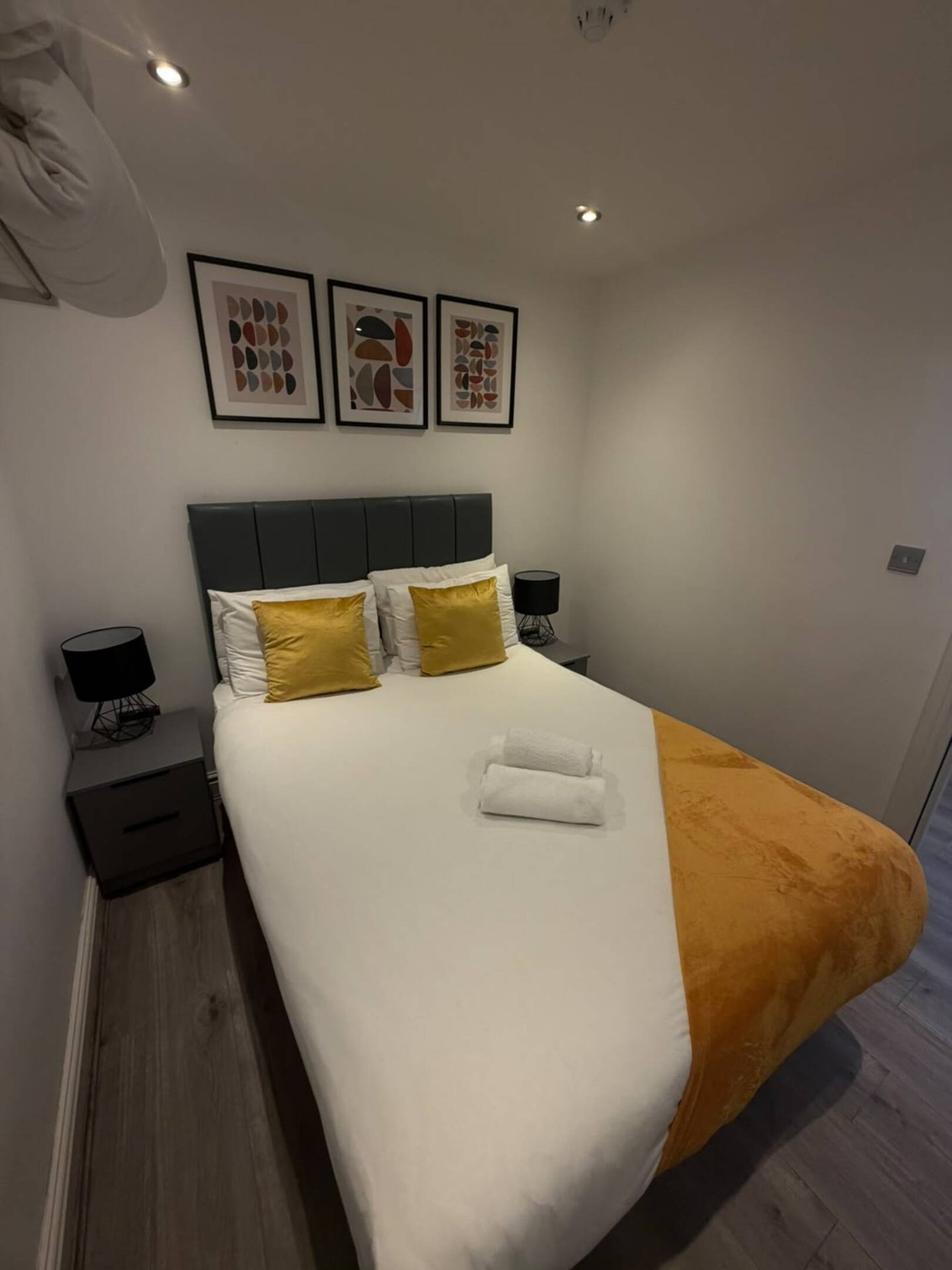 Modern bedroom with double bed, yellow cushions, white bedding, and framed wall art