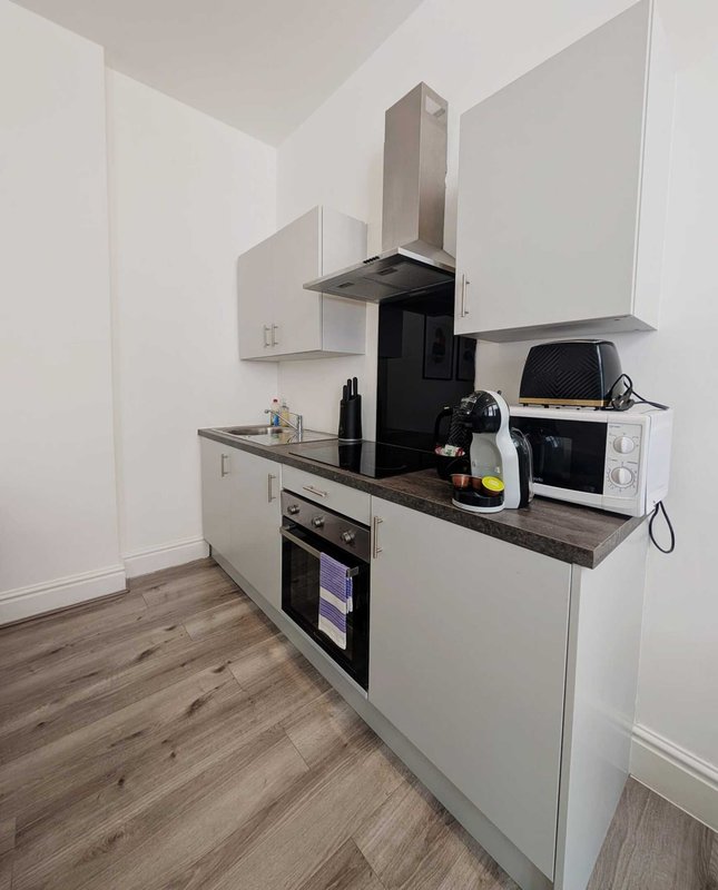 Modern kitchen with white cabinets, dark countertop, built-in appliances and hood vent