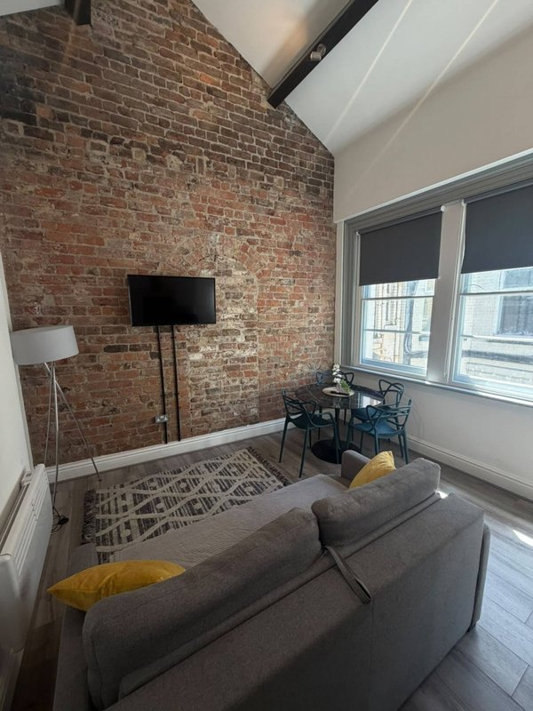 Modern living room with grey sofa, exposed brick wall, wall-mounted TV and large windows