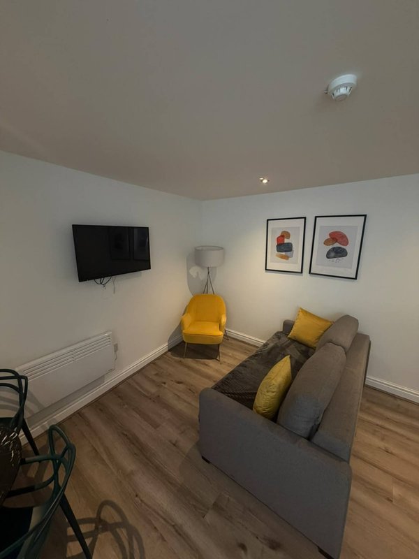 Living room with gray sofa, yellow cushions, wall-mounted TV, wooden flooring and framed wall art
