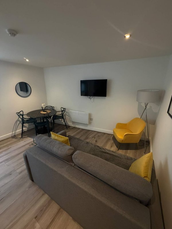 Open-plan living area with grey sofa, yellow armchairs, dining table, wall-mounted TV and floor lamp