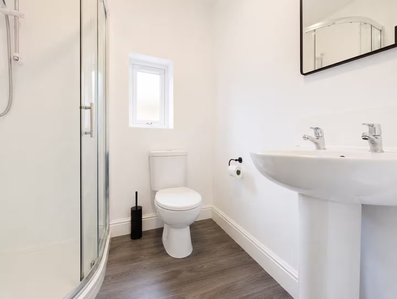 Clean modern bathroom with toilet, dual sink, shower enclosure and small window