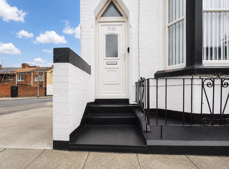 White and black exterior house entrance with black steps, metal railing and white door