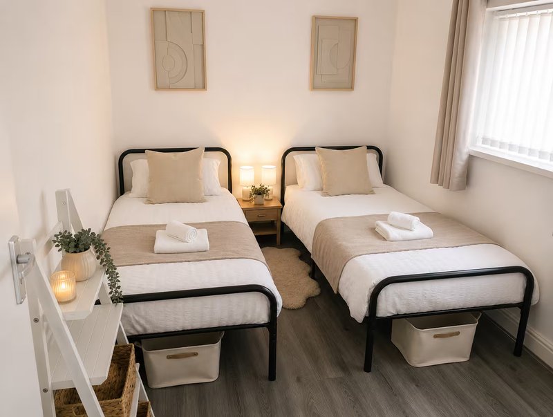 Twin bedroom with two single beds, white bedside table, neutral decor and window