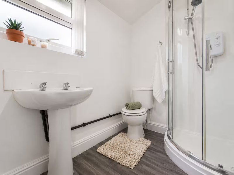 Clean bathroom with pedestal sink, toilet, shower cubicle and small window with plant