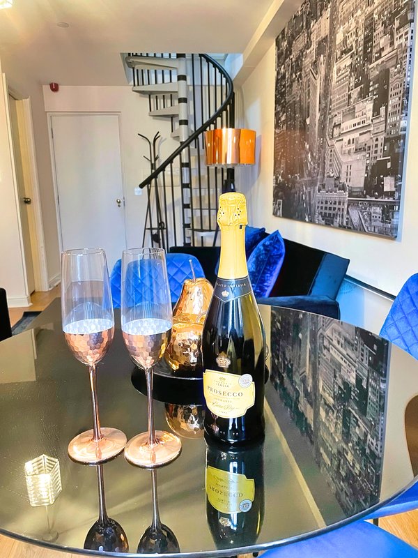 Modern dining area with champagne bottle, wine glasses, black spiral staircase and city photographs on walls