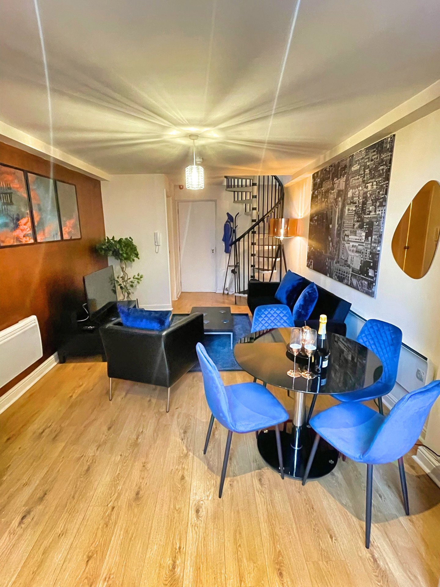 Open-plan living and dining area with blue chairs, wooden flooring, and staircase visible
