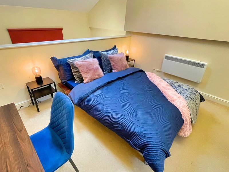 Modern bedroom with blue bedding, pink throw, bedside table, and accent lighting