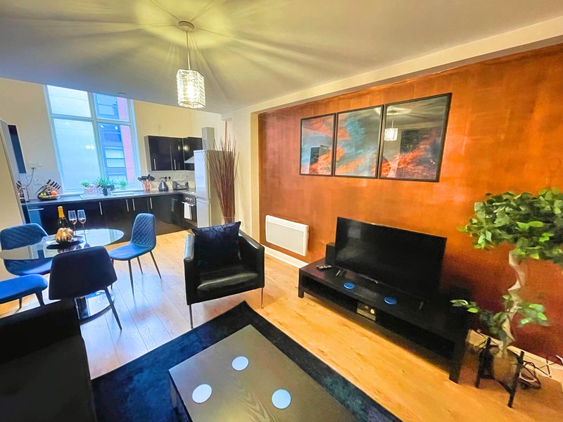 Modern open-plan living room with orange accent wall, dining area, TV stand and natural lighting