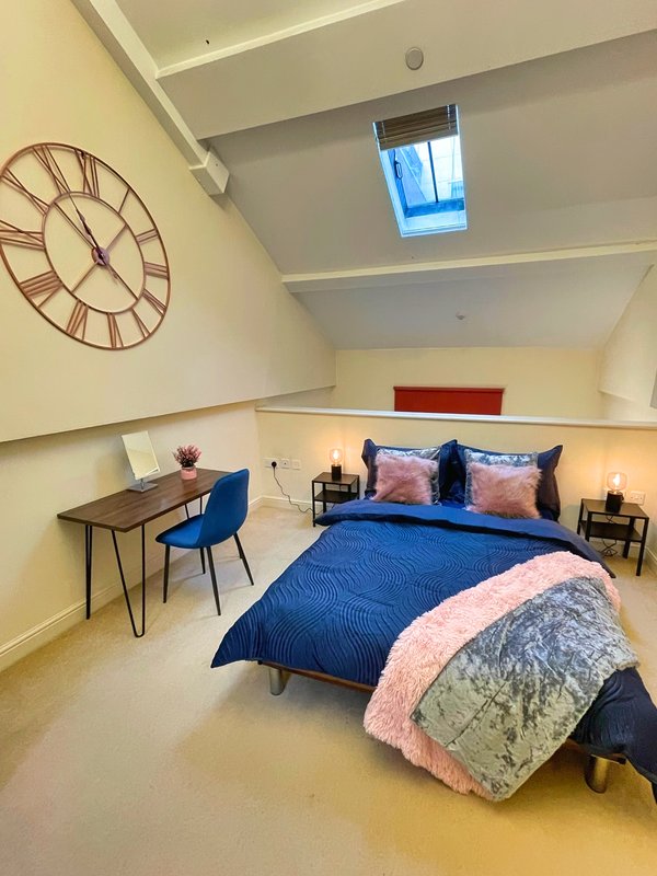 Modern bedroom with double bed, desk, blue chair, skylight window and decorative wall clock