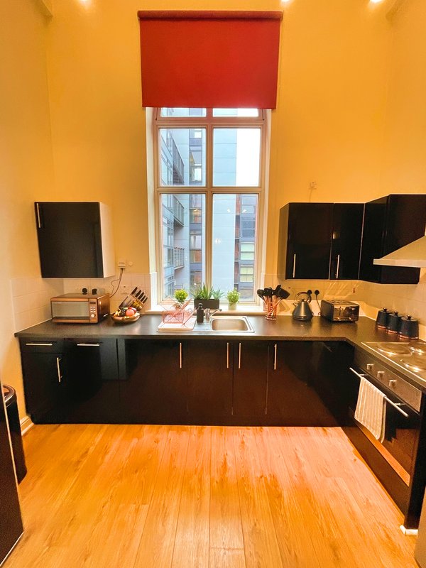 Modern kitchen with black cabinetry, bright yellow walls, window with red blind, wooden floor