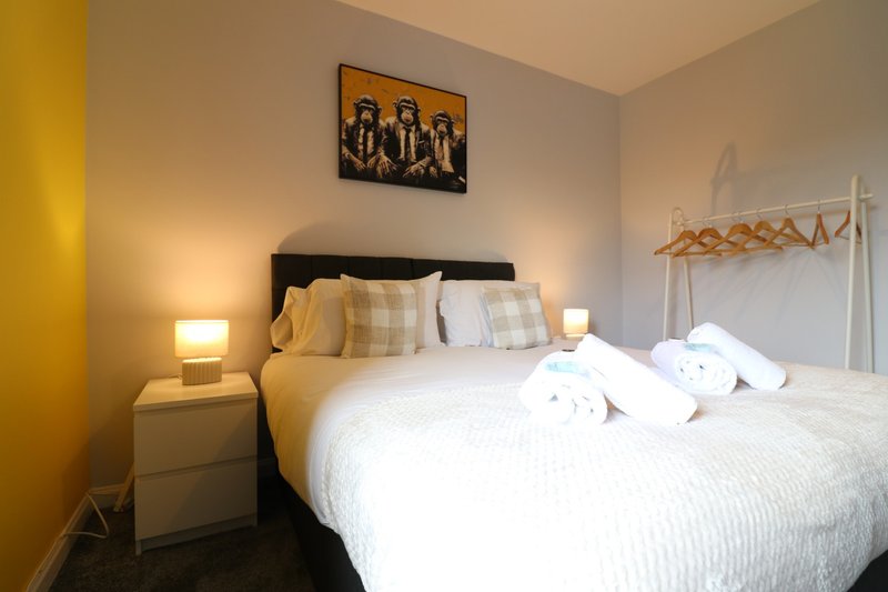Bedroom with double bed, black headboard, white bedding, side lamps, and wall art