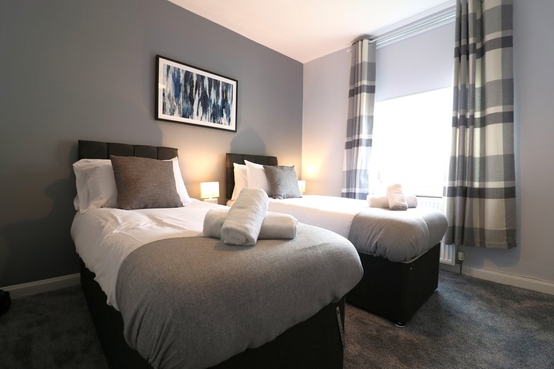 Twin bedroom with grey beds, pillows, bedside lamps and checked curtains