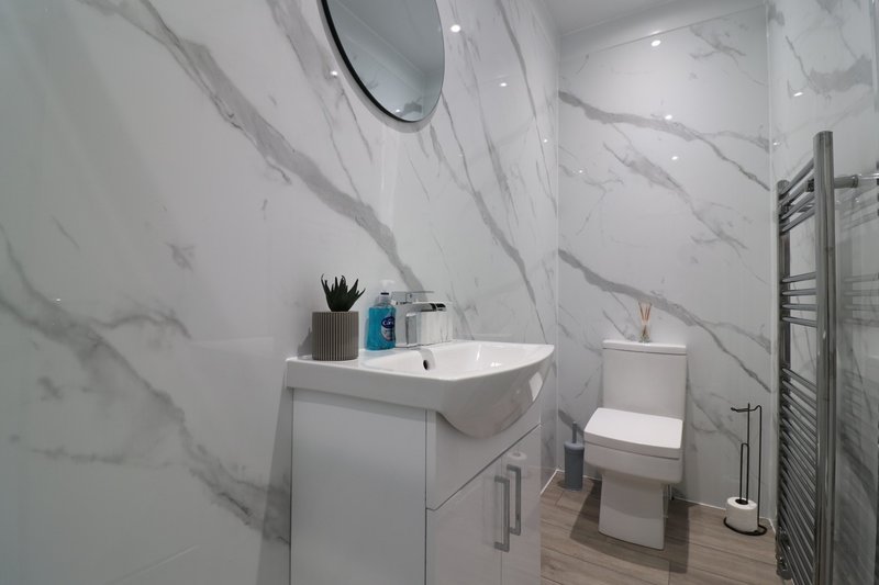 Modern bathroom with white marble-effect tiles, vanity sink, toilet and heated towel rail