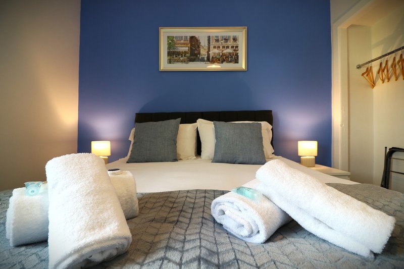 Bedroom with double bed, blue accent wall, white pillows and towels, bedside lamps