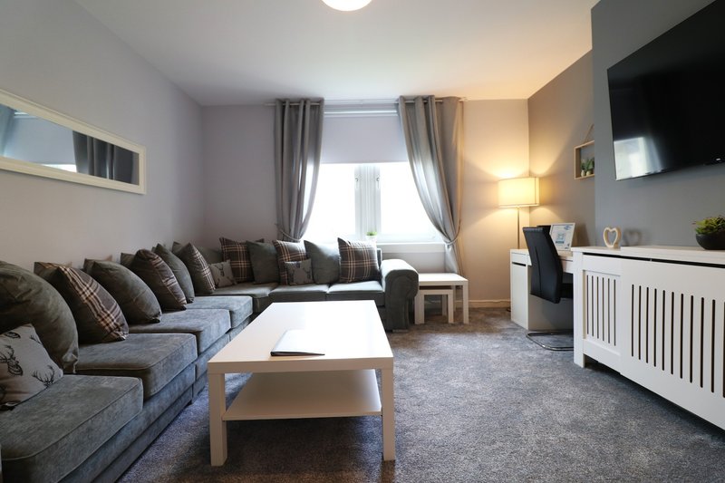Modern living room with grey sofa, coffee table, fireplace, and large windows with curtains