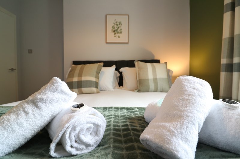 Bedroom with double bed, rolled white towels, patterned cushions and framed botanical art