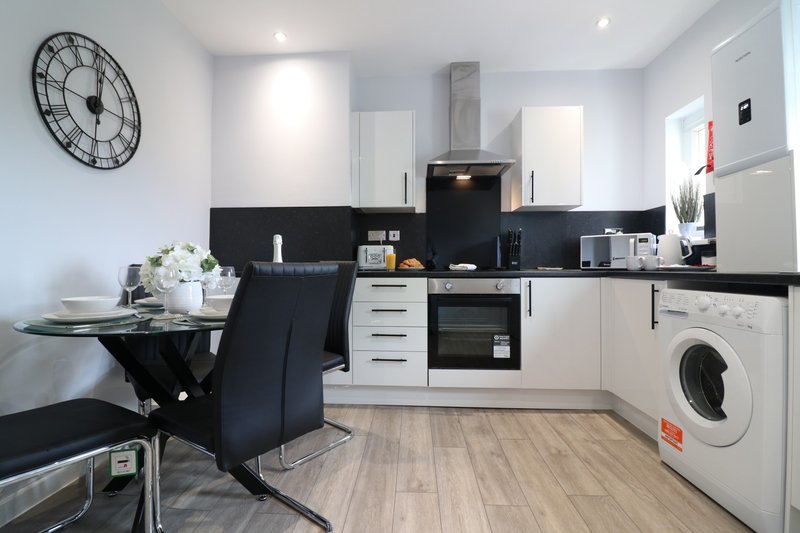 Modern kitchen with white cabinetry, black countertops, integrated appliances and dining area
