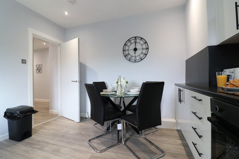 Modern open-plan kitchen and dining area with black dining table, white cabinetry, and wall clock