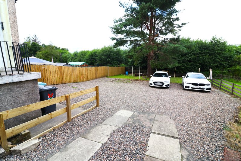Gravel driveway with parking spaces, wooden fence, patio area and mature trees