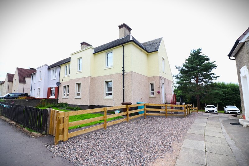 Yellow and cream rendered semi-detached house with wooden fence and gravel driveway