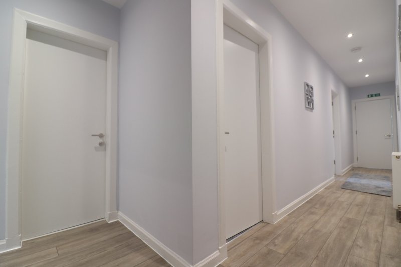 Bright hallway with white doors, light wood flooring and recessed ceiling lights