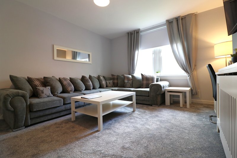 Modern living room with grey corner sofa, wooden coffee table, and large window with curtains