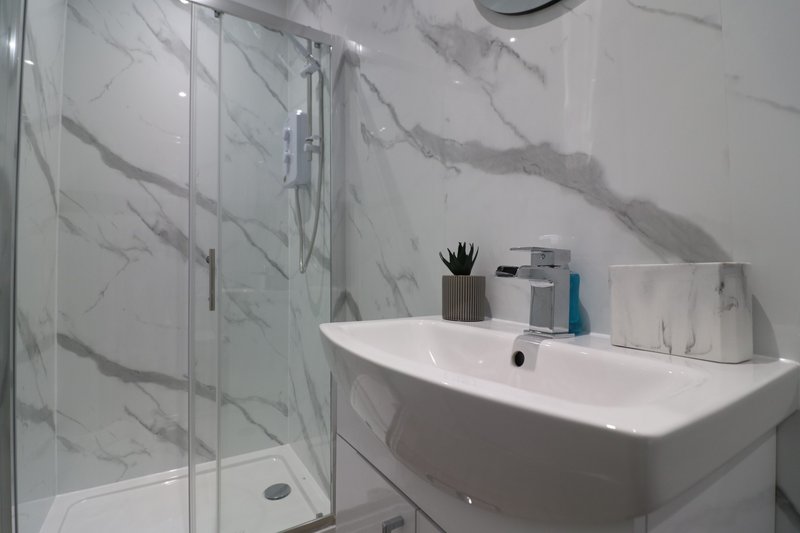Modern bathroom with marble-effect tiles, white sink, glass shower enclosure and toiletries