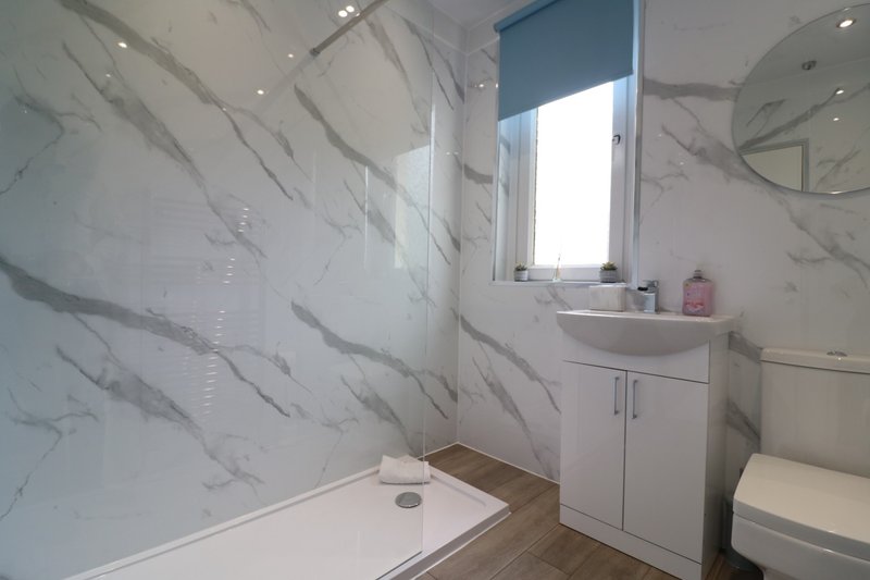 Modern bathroom with marble-effect tiling, walk-in shower, white vanity, and window