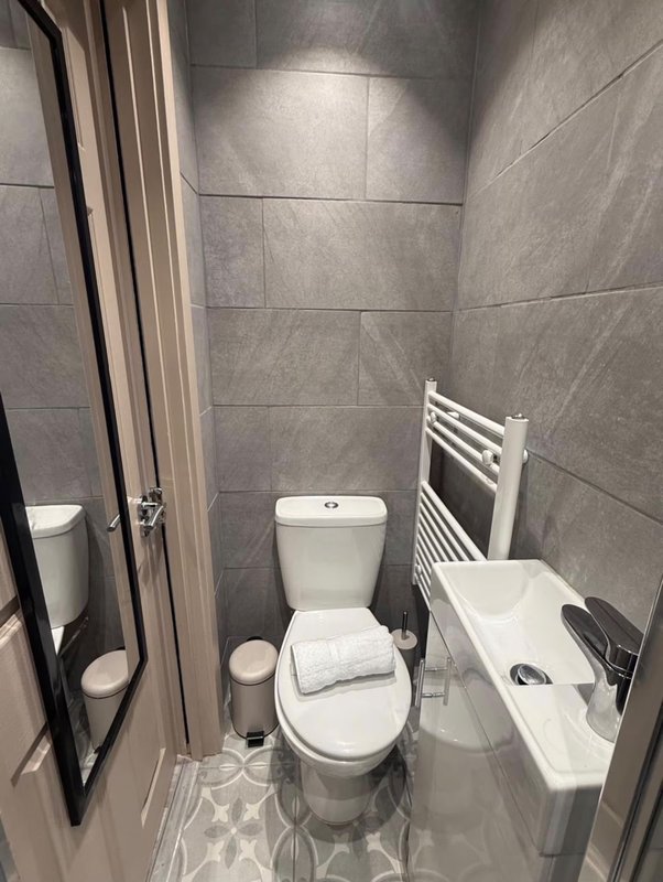 Modern bathroom with toilet, sink, towel rail, and grey tile walls