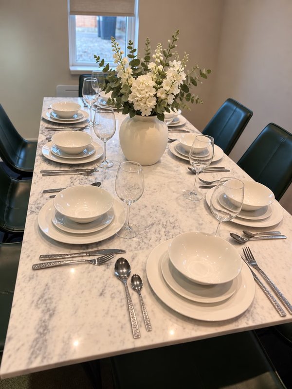 Formal dining table set with white plates, cutlery, flowers and window view
