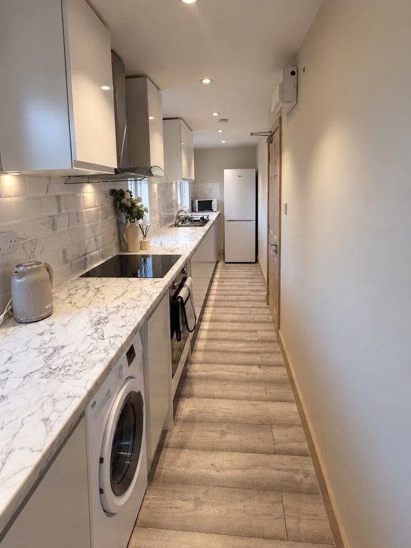 Modern galley kitchen with marble countertops, white cabinetry, stainless steel appliances and wooden flooring
