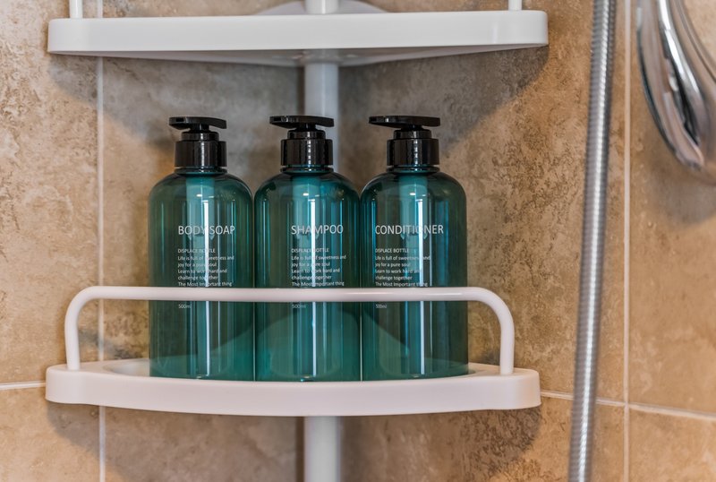 Bathroom shelf with three green pump bottles of toiletries and white towel rail