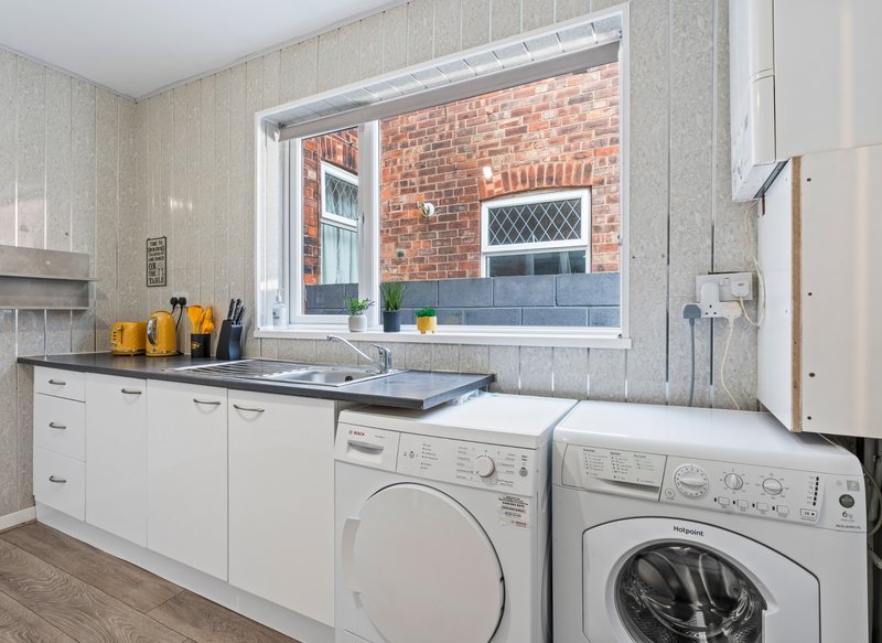 Kitchen and laundry room with white cabinets, sink, washing machine and dryer, window overlooking brick exterior