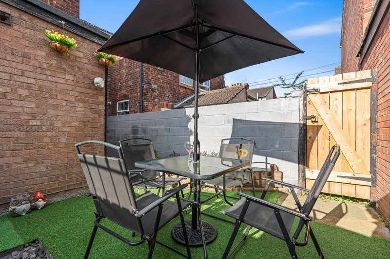 Compact garden patio with black umbrella, dining chairs, table and artificial grass