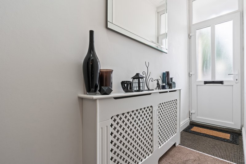 Entryway with white storage cabinet, decorative black bottle, mirror and potted plants