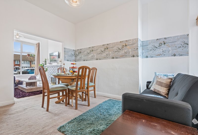 Open-plan living area with dining table, chairs, sofa, and kitchen visible through doorway